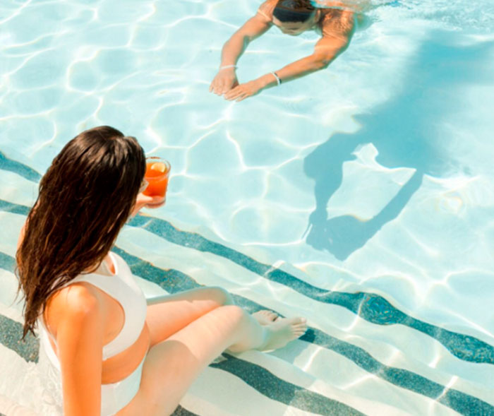 a woman sitting on the edge of a pool with a drink in her hand